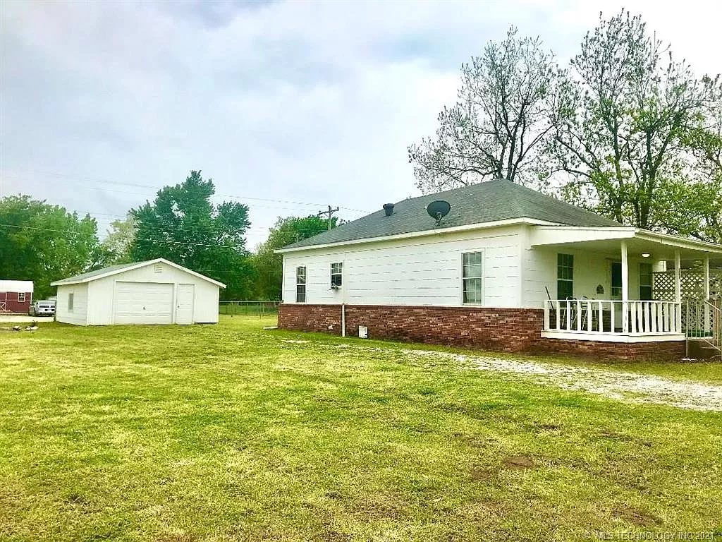 The house from the east — vinyl siding, brick skirt, covered front porch. Spring 2021.